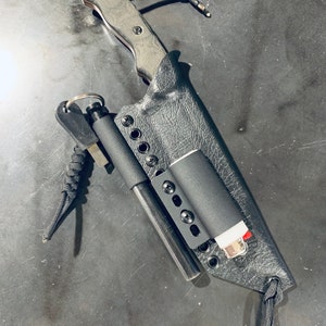 Puede incluir: Una funda de cuero negra con un cuchillo negro, un iniciador de fuego negro y un encendedor negro en su interior. La funda tiene un cord&oacute;n negro adjunto.