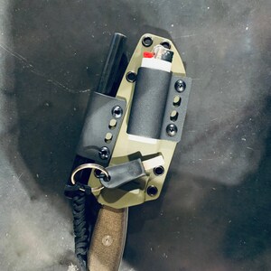 Puede incluir: Una funda de cuchillo verde con un iniciador de fuego negro, un encendedor negro y un cord&oacute;n de paracord negro.