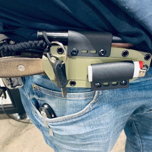 Puede incluir: Una persona que lleva pantalones vaqueros azules con una funda de cuchillo de cuero negro, un encendedor y un llavero sujetos a su cintur&oacute;n.