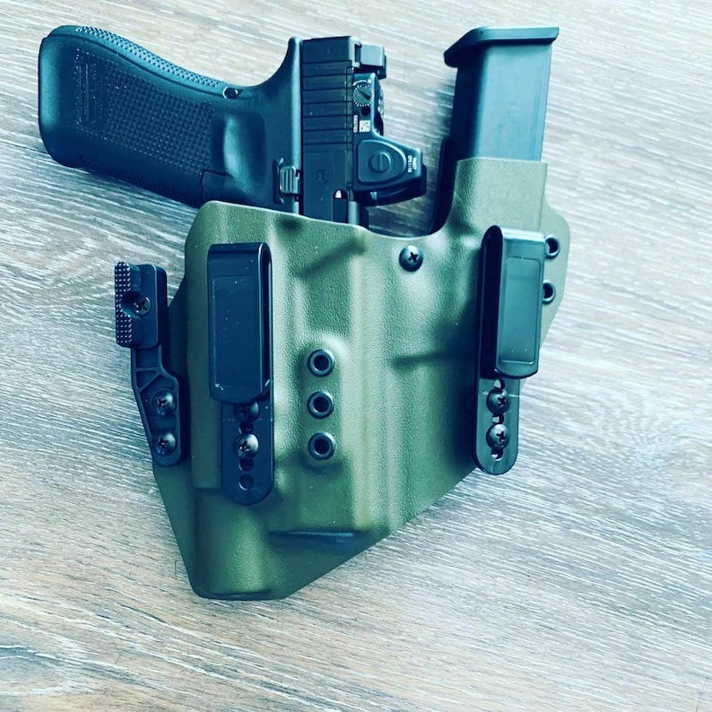 May include: A green leather holster with a black handgun and magazine inside. The holster has a black clip and a black adjustable retention screw.