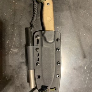 May include: A black leather knife sheath with a tan knife and a green cord attached. The sheath has multiple holes and a metal button.