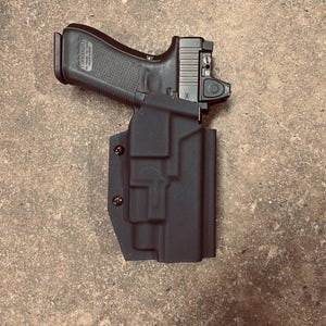 May include: A black handgun with a black holster. The holster has a textured surface and is secured with screws.
