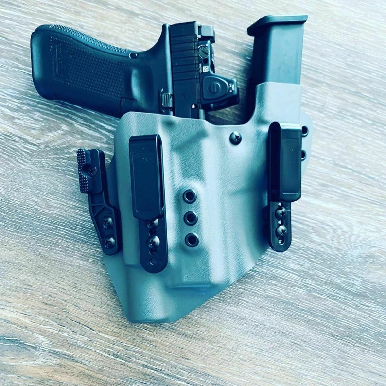 May include: A gray gun holster with a black clip and a black magazine holder. The holster has four small holes on the side.