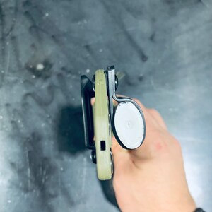 Puede incluir: Una funda negra y verde con un bot&oacute;n blanco. La funda est&aacute; hecha de un material pl&aacute;stico duro y tiene un bucle para el cintur&oacute;n.