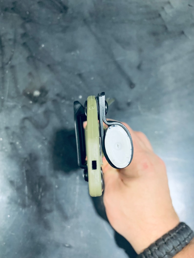 Puede incluir: Una funda negra y verde con un bot&oacute;n blanco. La funda est&aacute; hecha de un material pl&aacute;stico duro y tiene un bucle para el cintur&oacute;n.