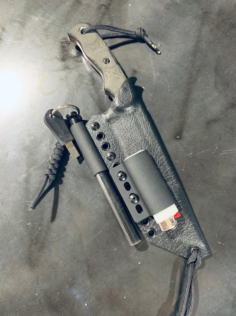 Puede incluir: Una funda de cuero negra con un cuchillo, un iniciador de fuego y un encendedor en su interior. La funda tiene una correa de paracord negra y un anillo de metal.