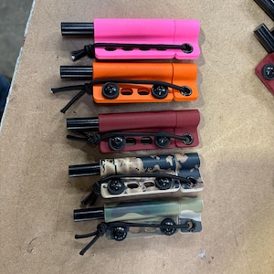May include: A collection of multi-colored, small, rectangular objects with a black cylindrical component and a black cord. Colors include pink, orange, burgundy, camouflage, and green camouflage.