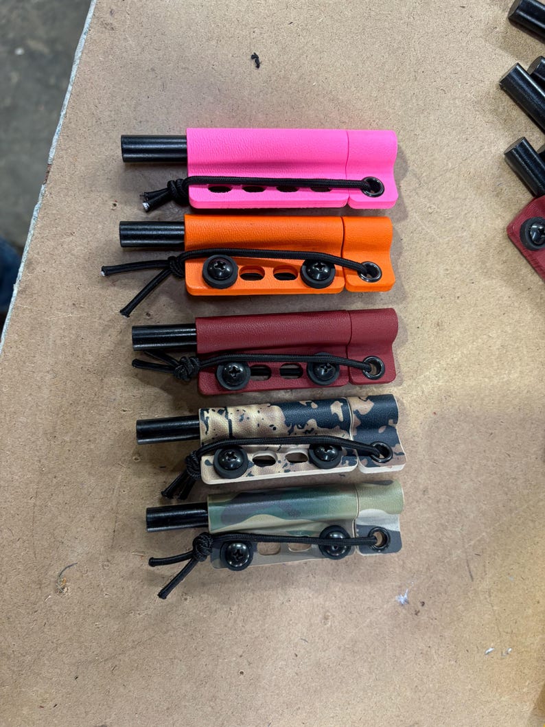 May include: A collection of multi-colored, small, rectangular objects with a black cylindrical component and a black cord. Colors include pink, orange, burgundy, camouflage, and green camouflage.