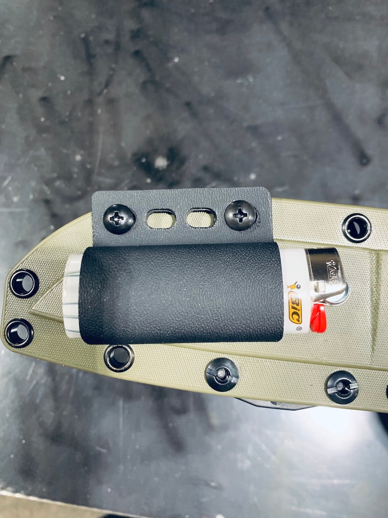 Puede incluir: Un porta mechero negro y gris con un mechero negro unido a un cuchillo verde. El porta mechero tiene dos tornillos a cada lado y tres agujeros en el medio. El mechero es un mechero BIC con un dise&ntilde;o rojo y amarillo.