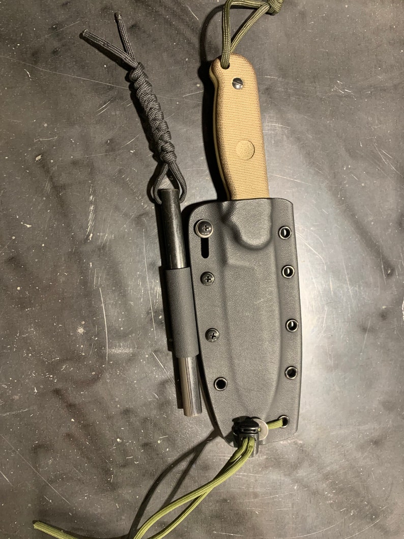 May include: A black knife sheath with a tan handle knife and a black fire starter inside. The knife and fire starter are attached to a green cord.