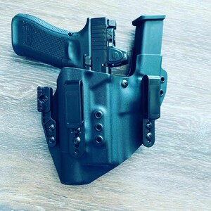 May include: A black gun holster with a black gun and magazine inside. The holster has a belt clip and multiple screws.