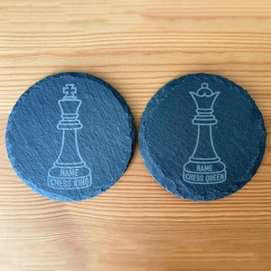 Może przedstawiać: Dwa okrągłe czarne podkładki ze łupka z białym obrysem króla i królowej szachowej. Podkładka króla mówi "NAME CHESS KING", a podkładka królowej mówi "NAME CHESS QUEEN".