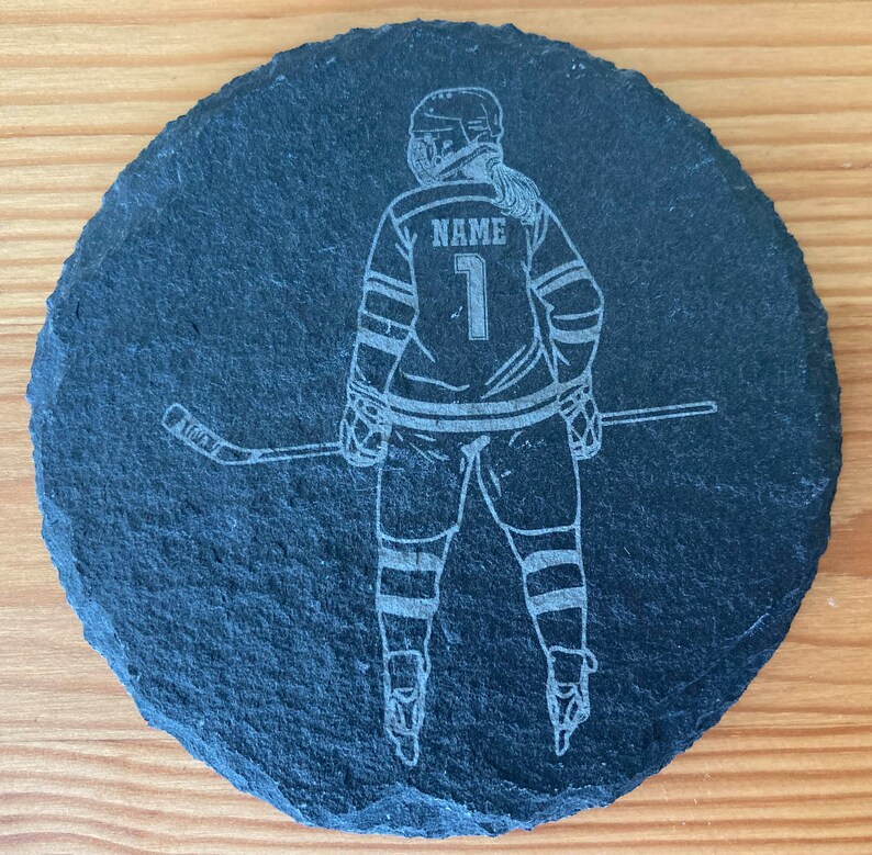 Puede incluir: Posavasos de pizarra negra con una silueta blanca de un jugador de hockey sosteniendo un palo. El jugador lleva una camiseta con la palabra "NAME" y el n&uacute;mero "1" en la espalda.