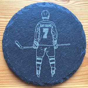 Puede incluir: Un posavasos de pizarra negra con una silueta blanca de un jugador de hockey sosteniendo un palo. La camiseta del jugador tiene el texto "ANY NAME" y el n&uacute;mero "7" en la espalda.