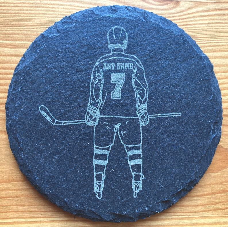 Puede incluir: Un posavasos de pizarra negra con una silueta blanca de un jugador de hockey sosteniendo un palo. La camiseta del jugador tiene el texto "ANY NAME" y el n&uacute;mero "7" en la espalda.