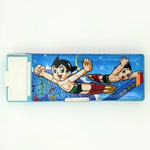 May include: A blue pencil case with a picture of Astro Boy flying in space. The case has a white latch and a silver metal clip. The text "미래만" is printed on the case.