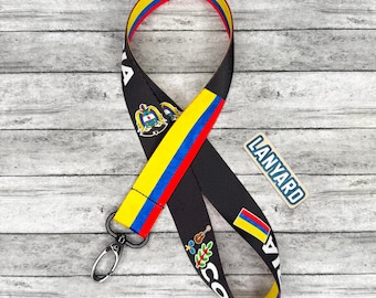 May include: Black lanyard with a colorful design featuring the colors of the Colombian flag: yellow, blue, and red. The lanyard has a metal clasp and the word "LANYARD" printed on a small rectangle.