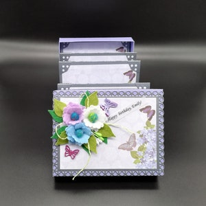 May include: A purple and gray layered card with a white background. The card has a decorative border and features a felt flower bouquet with butterflies and the text "Happy birthday, Emily!"