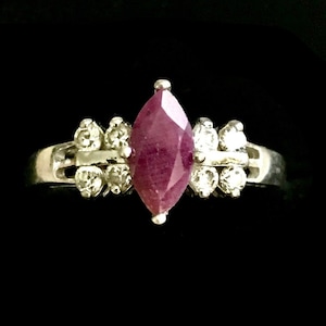 May include: A silver ring with a marquise-shaped ruby gemstone surrounded by smaller clear gemstones.