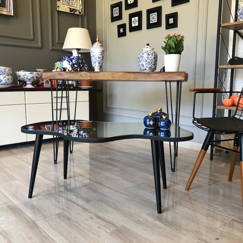 May include: A low coffee table with an irregular, kidney-shaped black glass top and three tapered black legs. The table features a reflective surface and a smooth, curved edge design, providing a stable base for decorative items in a living space.