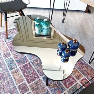 May include: An irregular, kidney-shaped coffee table with a reflective mirrored surface and a black edge. The table features dark wooden legs and displays several decorative ceramic pomegranate-shaped ornaments in shades of blue and teal.