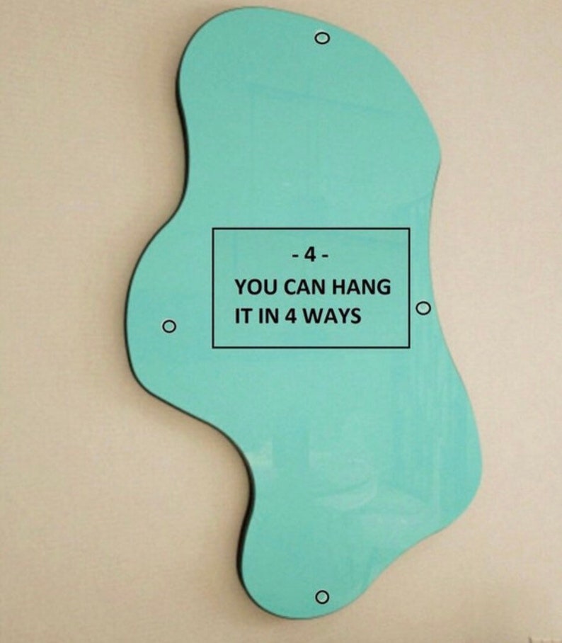 May include: An irregular, organic-shaped light teal mirror featuring four small circular mounting holes positioned along its perimeter. A rectangular black border in the center contains the text: - 4 - YOU CAN HANG IT IN 4 WAYS.