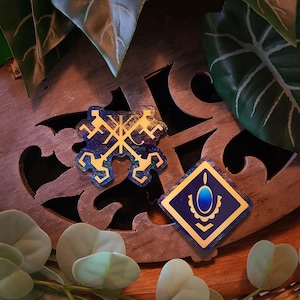 May include: Two gold and blue holographic stickers on a wooden surface. One sticker features a stylised design of four keys, the other features a blue gem in a gold frame.