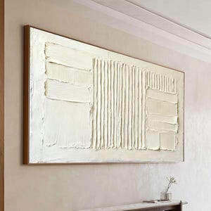 May include: Large, rectangular abstract painting with a textured, off-white surface. The artwork features a series of vertical and horizontal brushstrokes within a dark brown wooden frame. The painting is mounted on a light beige wall above a dark brown bench.