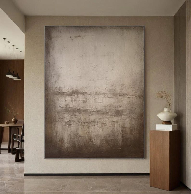 May include: Abstract painting with a textured, layered effect in shades of brown and beige. The painting is displayed on a wall in a modern interior.