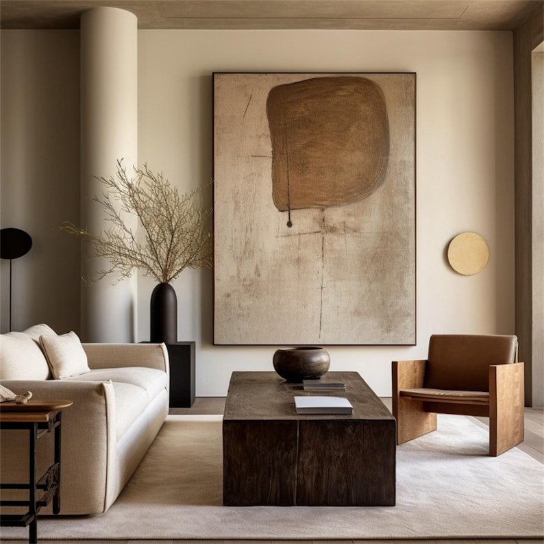May include: A modern living room with a beige sofa, a wooden coffee table, a brown armchair, and a large abstract painting on the wall. The painting features a brown shape on a beige background.