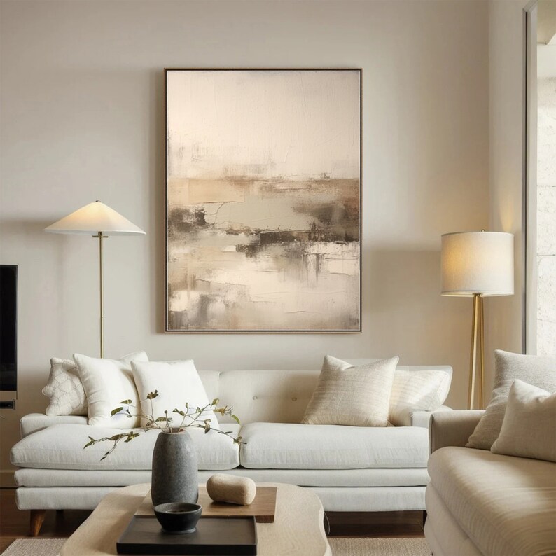 May include: Abstract landscape painting in shades of brown, beige, and white. The painting is framed and hanging on a wall in a living room setting.
