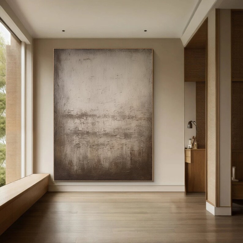 May include: A large abstract painting in shades of brown and white hangs on a wall in a modern interior. The painting has a textured surface and a subtle horizontal pattern.