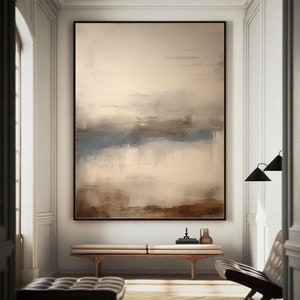 May include: Abstract painting with a beige background and brown, blue, and gray brushstrokes. The painting is framed in a black frame and is hanging on a white wall.