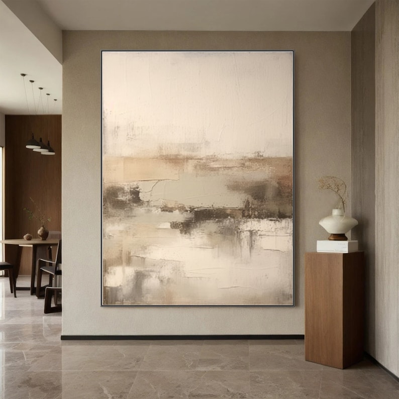 May include: Abstract painting with shades of beige, brown, and gray. The painting has a textured, layered look, with brushstrokes visible throughout. The painting is framed in a thin black frame.