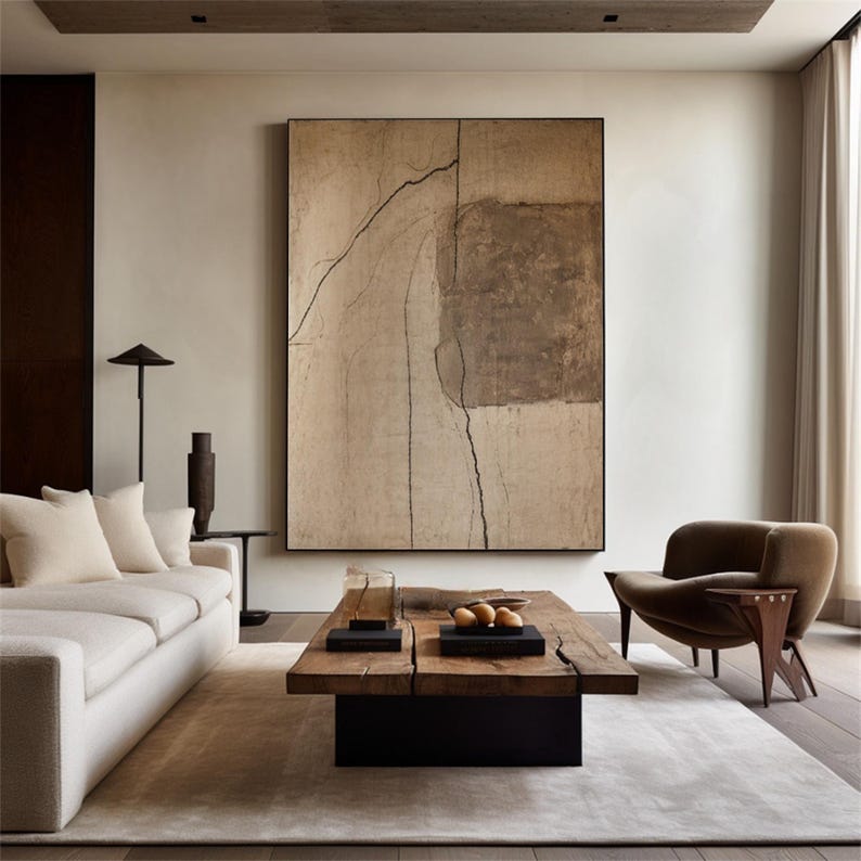 May include: A modern living room featuring a large abstract painting with a black frame. The room includes a white sofa, a wooden coffee table, and a brown armchair. The color palette is neutral, with beige, brown, and black tones.