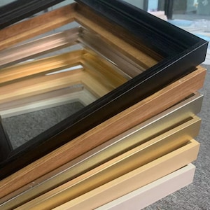 May include: A stack of picture frames in various colors and styles, including black, wood, gold, and white.