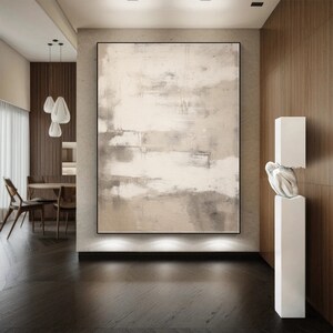 May include: Abstract painting in shades of beige and gray with a white background. The painting is hanging on a wall in a modern interior with wooden paneling and a white sculpture.