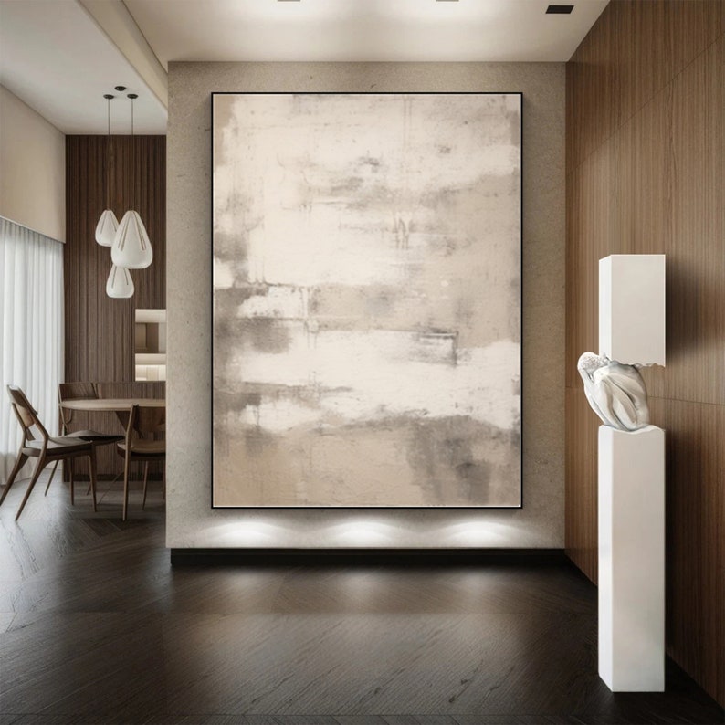 May include: Abstract painting in shades of beige and gray with a white background. The painting is hanging on a wall in a modern interior with wooden paneling and a white sculpture.