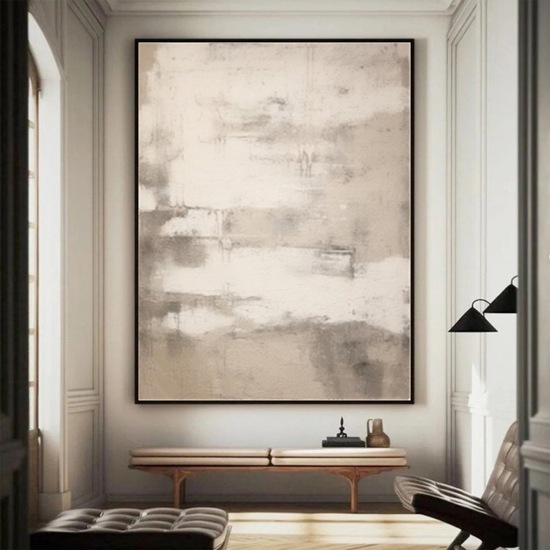 May include: Abstract painting with shades of beige and white. The painting is framed and hanging on a white wall in a modern interior.