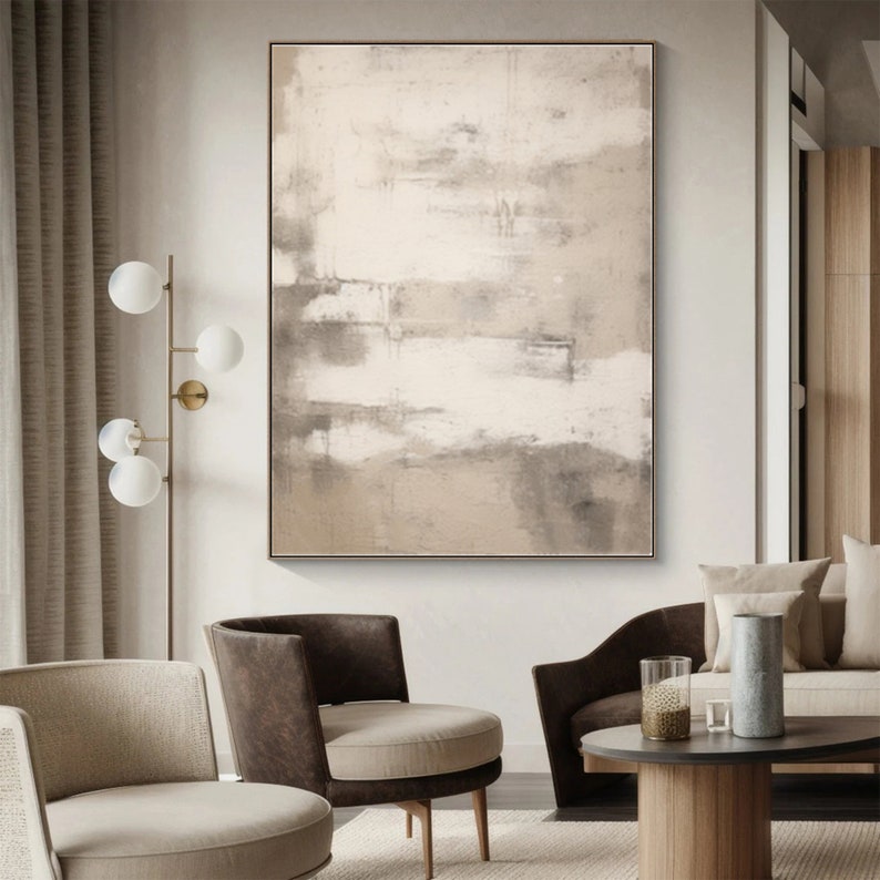 May include: Abstract painting with shades of beige, brown, and white. The painting is framed and hanging on a white wall in a living room setting.