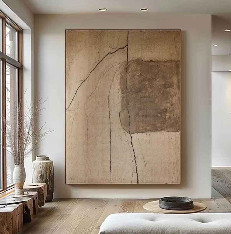 May include: Large abstract painting in neutral tones. The artwork features a textured beige background with a dark brown rectangular shape and black linear details. The painting is framed in a simple wooden frame and hangs on a white wall.