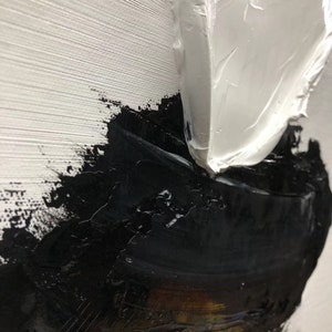 May include: Abstract painting with thick white and black paint strokes. The white paint is applied in a thick, textured layer, while the black paint is applied in a more fluid, layered style. The painting has a modern and abstract feel.