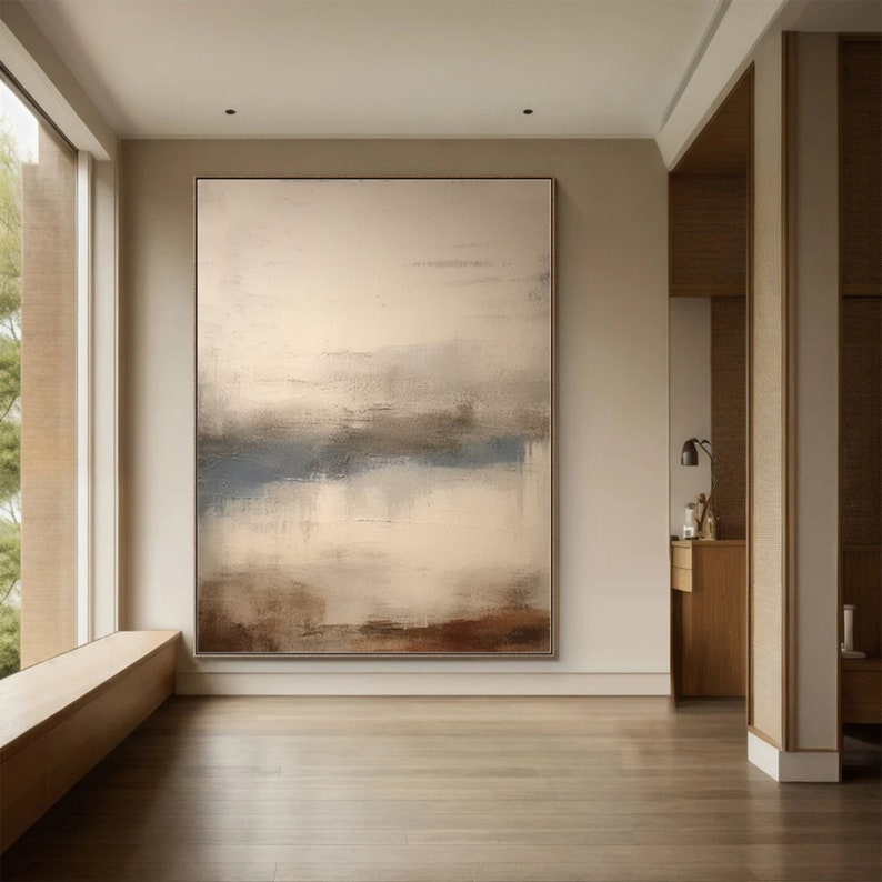 May include: Abstract painting with a horizontal band of blue, brown, and white on a white background. The painting is framed and hanging on a wall in a modern interior.