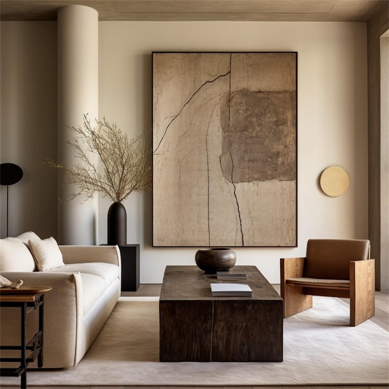 May include: A modern living room with neutral tones. Features a cream-colored sofa, a wooden coffee table, and a brown leather chair. A large abstract painting hangs on the wall, and a tall black vase holds dried branches.