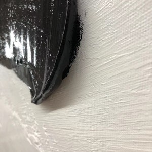 May include: Close-up of a black abstract painting on a white textured canvas.