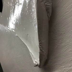 May include: Close-up of a white textured wall with a thick layer of white paint applied in a textured, uneven pattern.