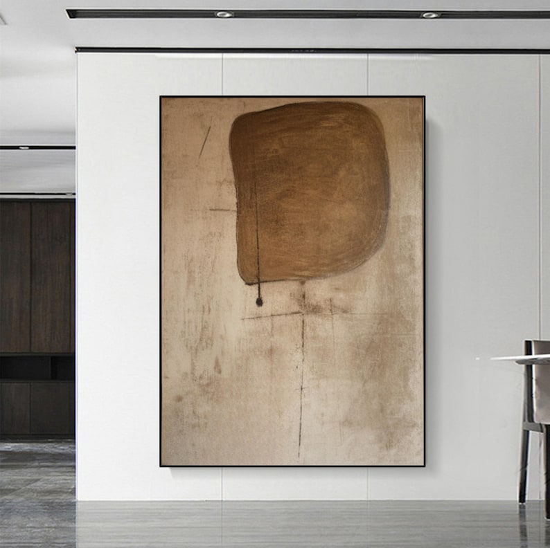 May include: Abstract art print featuring a large brown shape with a black dot in the center, on a beige background with subtle lines.
