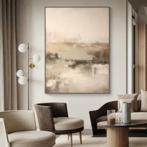 May include: Abstract painting with brown, beige, and green hues. The painting is framed and hanging on a white wall in a living room setting.