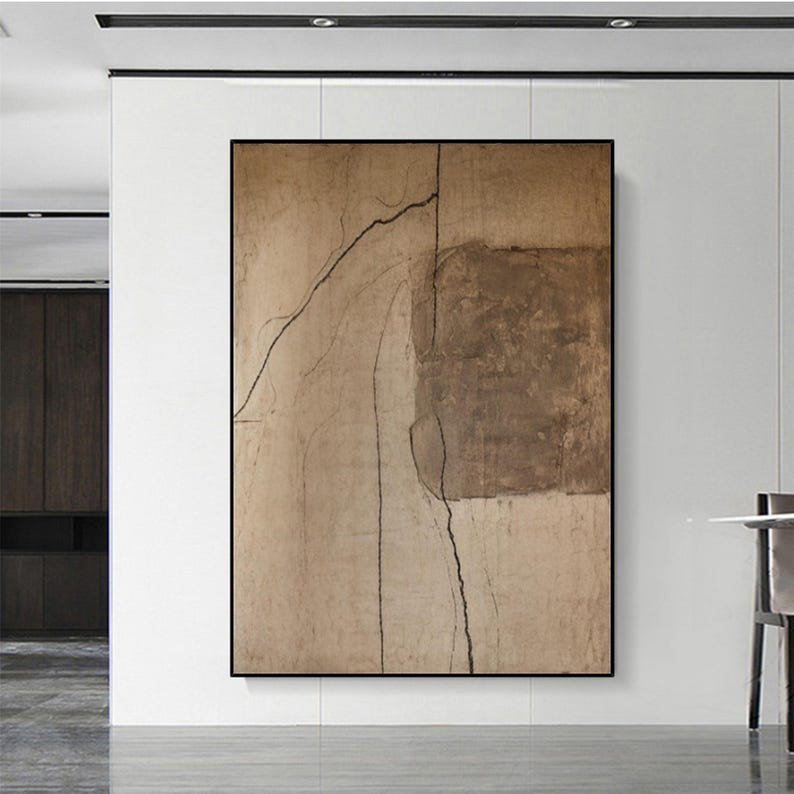 May include: Abstract art piece in a black frame. The artwork features a textured, neutral color palette with shades of beige and brown. Dark, linear elements create a contrast against the lighter background, adding depth and visual interest to the composition.