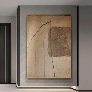 May include: Abstract art piece in a gold frame. The artwork features a textured beige background with a large brown square on the right side. Black lines create a network of shapes across the canvas. The artwork is displayed on a gray wall.